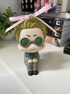 a figurine is sitting on a table with books in the background and a pink ribbon tied to it's head