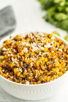 a white bowl filled with corn and feta cheese on top of a table next to vegetables