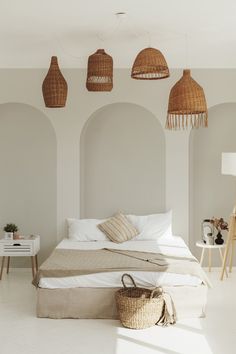 a bed with white sheets and pillows in a room that has three hanging lights above it