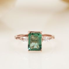 an emerald and diamond ring sitting on top of a table