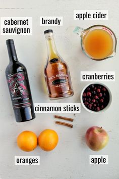 the ingredients to make an apple cider recipe are shown on a white surface, including apples, cinnamon sticks, cranberries, oranges, and maple syrup