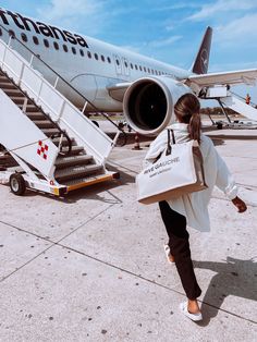 a woman is walking towards an airplane with her hand in her pocket and carrying a bag