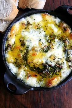 a skillet filled with cheese and spinach on top of a wooden table next to bread