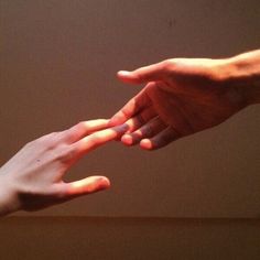 two people reaching out their hands to touch each other's hand, with sunlight shining on the wall behind them