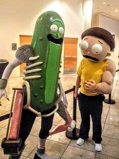 two people standing next to each other in front of a giant pickle and man