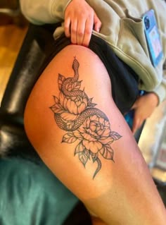 a woman's thigh with a tattoo on it and flowers around the leg area