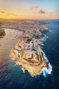 an aerial view of the city and its coastline at sunset, with boats in the water