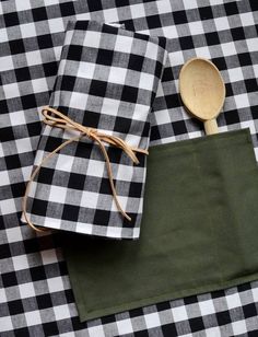 a black and white checkered table cloth with two wooden spoons in it next to a green napkin