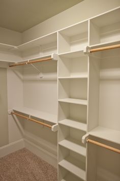 an empty walk in closet with white shelving and wooden rails on the wall,