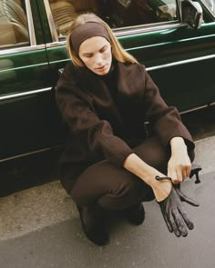 a woman sitting on the ground next to a green car with her hands in black gloves