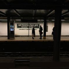 two people are standing on the platform waiting for their train to arrive at night time