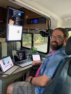 a man sitting at a desk in the back of a truck with two laptops on it