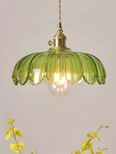 a green glass light hanging from a ceiling fixture with yellow flowers in the foreground