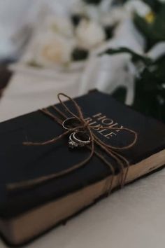 a book with two rings tied to it sitting on a table next to some flowers