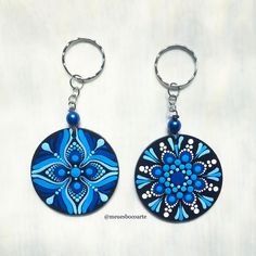 two circular key chains with blue and white designs on them, hanging from metal hooks