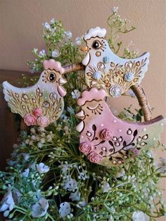 two wooden birds sitting on top of flowers