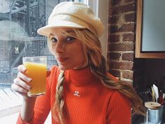 a woman in an orange sweater and hat holding a glass of orange juice