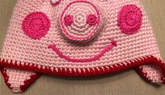 a crocheted hat with a smiling face on the front and sides, made to look like a pig