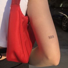 a person with a small tattoo on their arm holding a red bag and wearing a white shirt