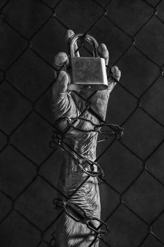 a hand holding a padlock in front of a chain link fence with barbed wire