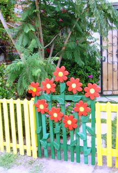 a fence with flowers painted on it and some plants in the back ground behind it