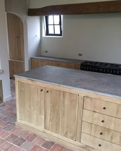 an empty kitchen with wooden cabinets and grey counter tops, along with brick flooring