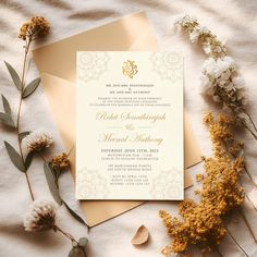 an elegant wedding card with gold foil on it and some flowers next to the envelope