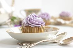 a cupcake with purple frosting sitting in a bowl next to two spoons