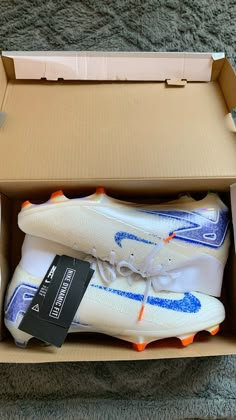 a pair of white and blue soccer shoes in a cardboard box on the carpeted floor