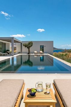 two lounge chairs sitting next to a pool with an olive tree in the middle of it