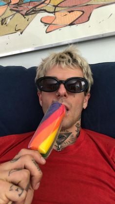 a man wearing sunglasses and holding a rainbow popsicle in his mouth while laying on a couch