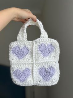 a hand holding a crocheted white purse with purple hearts on the front and sides