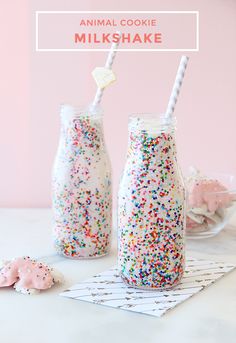 two milk bottles filled with sprinkles on top of a white table next to cookies