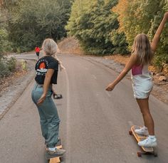 two young women riding skateboards down a road