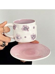 a person holding a coffee cup and saucer in their hands, with another hand on the plate