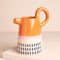 an orange and white ceramic pitcher sitting on top of a table next to a napkin