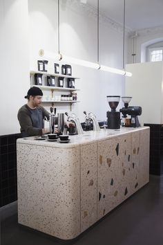 a man sitting at a counter in front of a coffee maker and other items on shelves