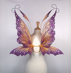 a white mannequin with purple and gold butterfly wings