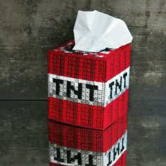 a red and white tissue box sitting on top of a wooden floor next to a wall