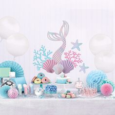 a table topped with lots of desserts and balloons in the shape of mermaid's tail