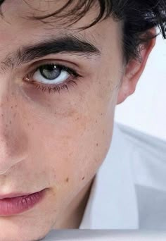 a young man with freckled hair and blue eyes looks at the camera while wearing a white shirt