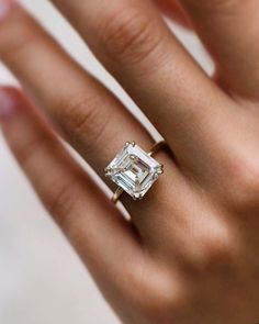 a woman's hand with a diamond ring on her left hand and an emerald stone in the middle