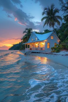 a house sitting on top of a sandy beach next to the ocean at sunset with palm trees