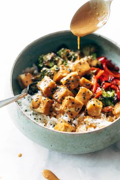 a spoon is being drizzled over rice with tofu and broccoli