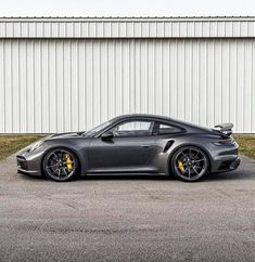 a grey porsche sports car parked in front of a building with a white wall behind it