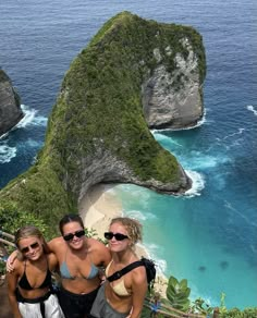 three women posing for a photo in front of the ocean and two large rock formations