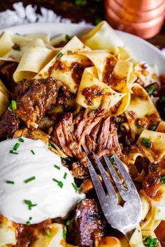 a white plate topped with pasta and meat covered in sauce, sour cream and parsley