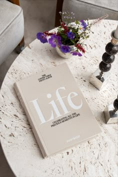 a book sitting on top of a white table next to a vase with purple flowers