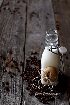 a glass bottle filled with milk and coffee beans on top of a wooden table next to a cookie