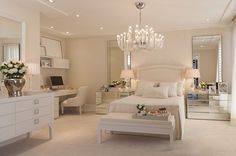 a white bedroom with a chandelier, bed and desk in the middle is shown